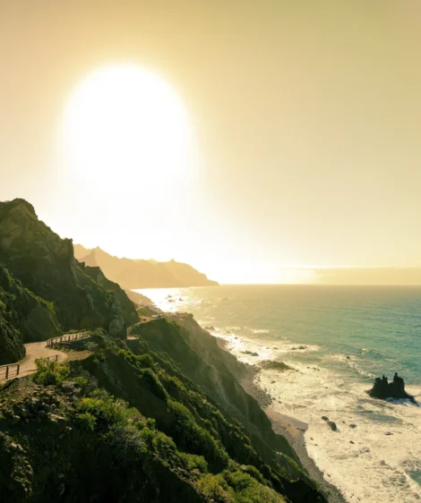 Beach With Fence and Body of Water With Hill and Sun in the Background