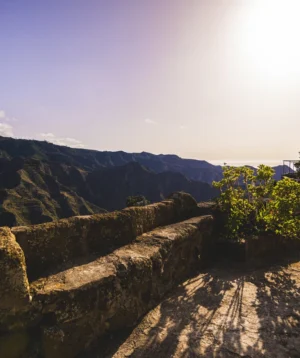 Rocky Cliff With Tree and Mountains in the Background