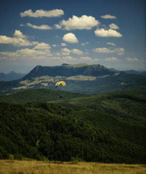 Person in the Air With Parachute Above Trees and Mountains